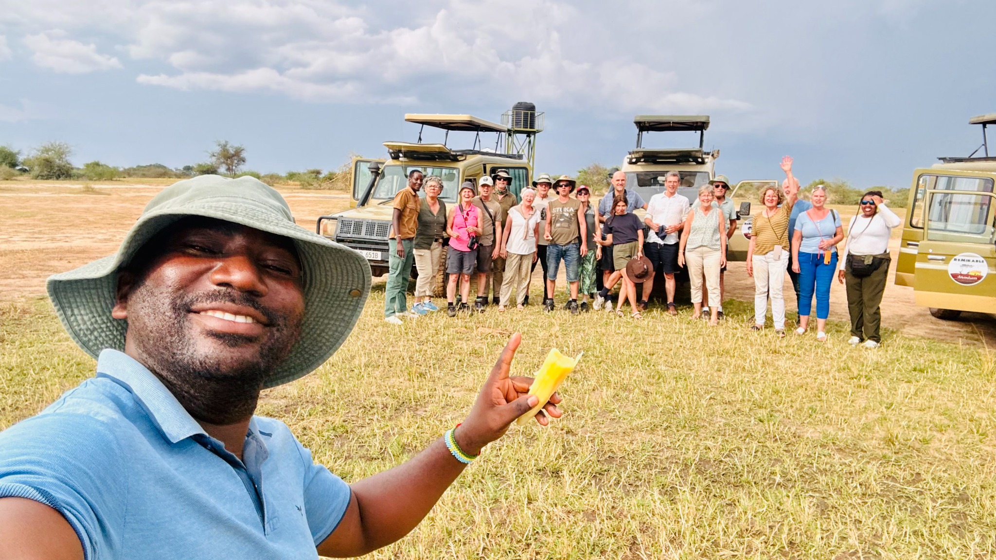 Group of travellers on safari with guide and vehicles in the background